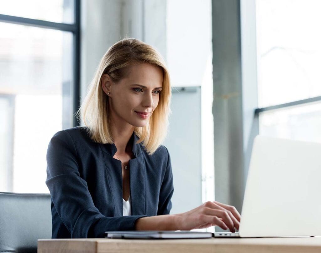 Smiling woman sitting at her desk working on a laptop.