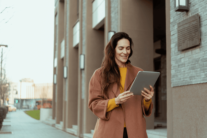 woman holding a tablet, walking in a city