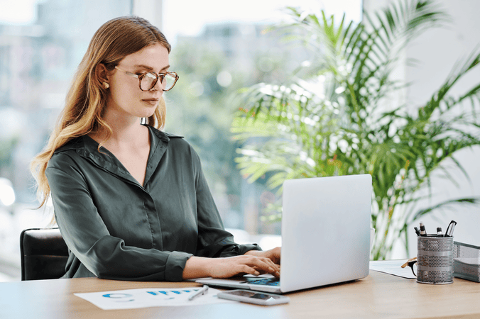 woman sitting at desk in an office, typing on a laptop